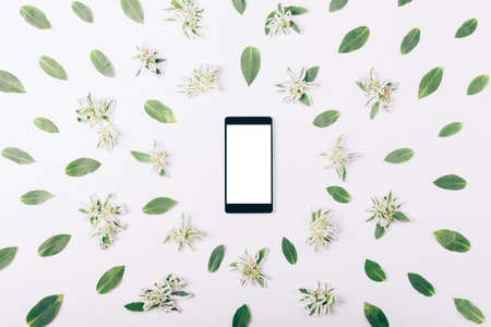 Mobile phone with blank screen among green leaves on a white background
