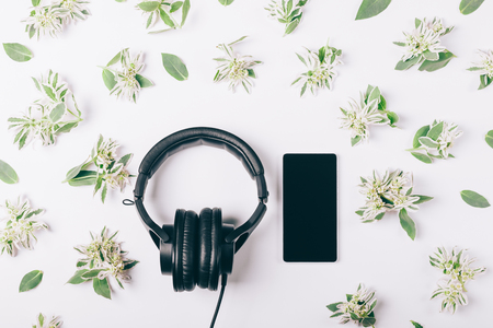 Headphones and mobile phone on a white table among green flowers top viewの写真素材