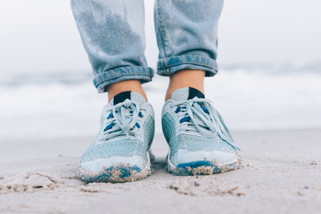 Female feet in wet jeans and sneakers on the beach close-upの写真素材