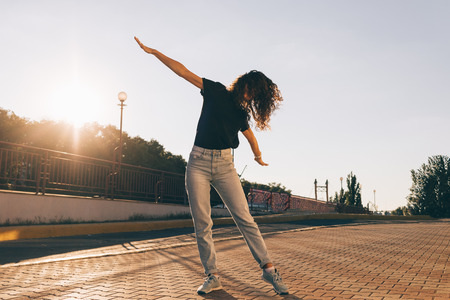 Beautiful slender girl with curly hair dancing in the city at sunset