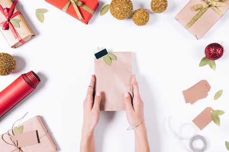 Women's hands are holding a package with a gift on a white table among Christmas decorations top viewの写真素材