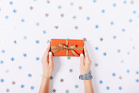 Beautiful female hands holding a red box with a gift on a white background among decorative snowflakes, top viewの写真素材