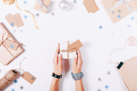 Beautiful female hands holding a small white box with a gift on a white background among the Christmas decorations, top viewの写真素材