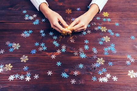 Sparkler in female hands and decorative snowflakes on the table, top viewの写真素材