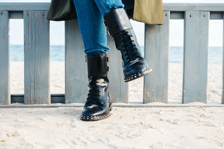 Close-up of female legs in black boots and jeans on the beach in winterの写真素材
