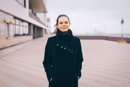 Young attractive woman in a black coat in a cloudy day