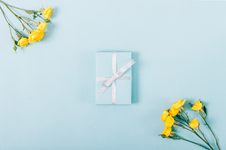 Bouquets of yellow roses and a gift box with a bow on a blue background top viewの写真素材