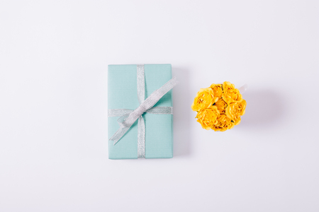 Yellow small roses and blue gift box with a bow on a white table top viewの写真素材