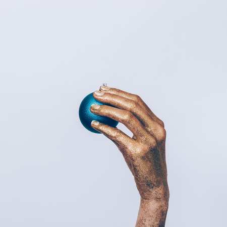 Female hand in a gold paint hold a blue Christmas tree ball on a white backgroundの写真素材