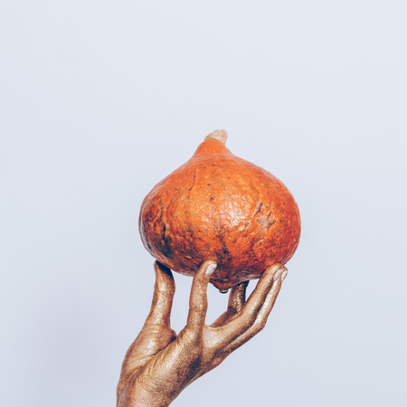Woman's hand in golden paint holding an orange pumpkin on a blue backgroundの写真素材