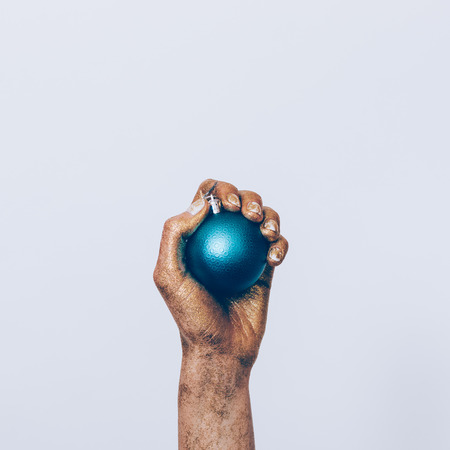 Close-up of a woman's hand in golden paint holding a blue Christmas ball on a white backgroundの写真素材