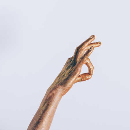 Posing female hand in golden glitter with white manicure on a gray backgroundの写真素材
