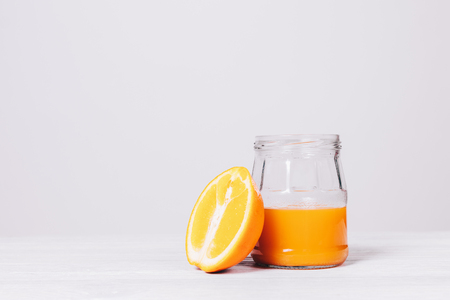 Cut orange and fresh juice in a glass jar on a white wooden tableの写真素材