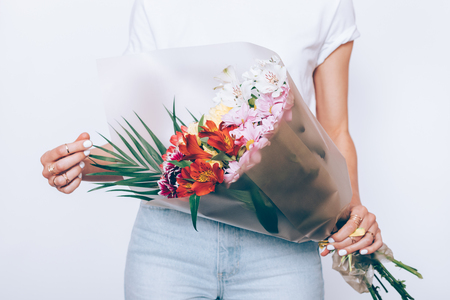 Slender girl in jeans and a T-shirt is holding a bouquet of flowers on a white backgroundの写真素材