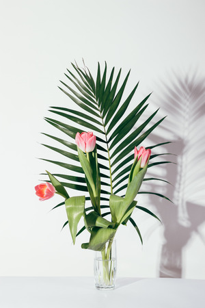 Pink tulips and palm leaf in a glass on a table, vertical framingの写真素材
