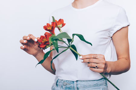 Slender woman in a T-shirt and jeans holds a bouquet of red flowers on a white backgroundの写真素材
