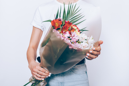 Woman in jeans and a T-shirt is holding a bouquet of flowers on a white background, close-upの写真素材
