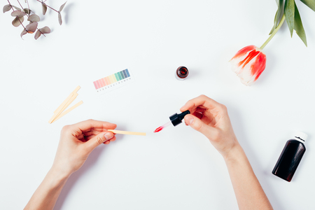 Woman testing cosmetics by using litmus paper. Top view of female hands on white background, applying with a pipette serum into a litmus test paper. Determination of pH level in cosmetics. Flat lay composition.の写真素材