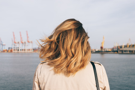 Close-up female head with golden honey color curly hairstyle watch at the seaport. Rear view young woman looking at the sea.の写真素材