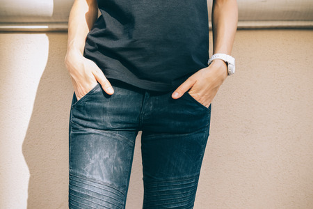Close-up of slender young female wearing white wristwatch, plain black t-shirt and jeans standing...