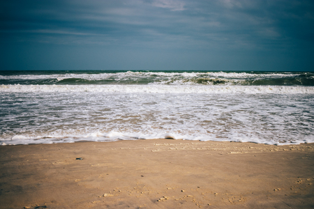 Overcast sea shore landscape. Ocean waves with foam lapping on the sandy beach under dark low clouds.の写真素材