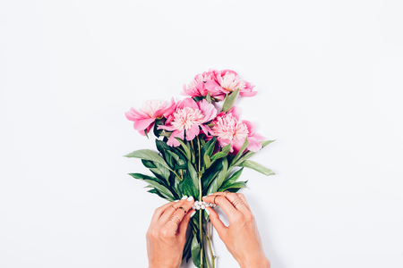Women's hands decorate a bouquet of pink peony flowers with  pearls, top view. Flat lay minimal composition with copy space.の写真素材