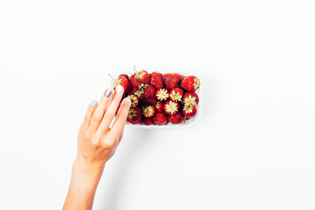 Woman picking strawberry from the basket, top view. Flat lay composition of female's hand taking one red berry on white background.の写真素材