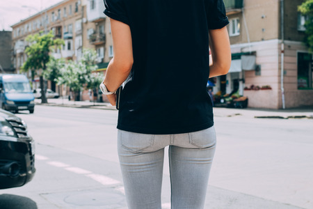 Slender young woman standing in front of the urban road with cars, rear view.の写真素材