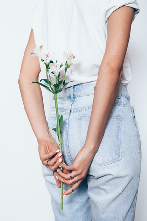 Rear view of young woman wearing high waisted boyfriend jeans holding sprig of lily standing on white background.の写真素材