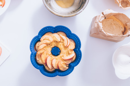 Silicone form with homemade traditional apple pie near ingredients and kitchenware on white table,...