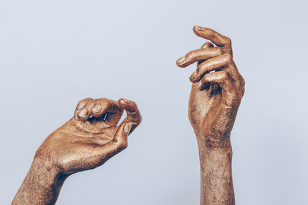 Beautiful female hands in golden paint with glitters make dancing gestures on plain background.の写真素材