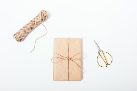 Gift just wrapped in brown eco paper near twine coil and golden scissors, top view. Flat lay...