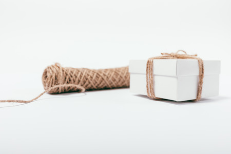 Gift tied with jute rope near twine coil. Close-up handmade packaged present on white table.の写真素材