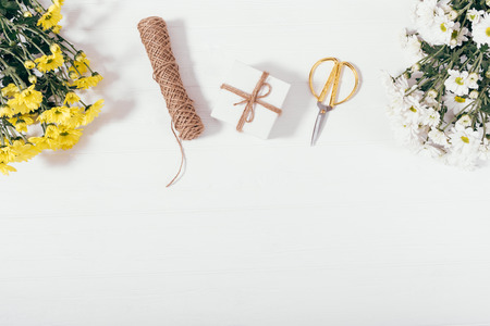 Flat layout of tied present box next to bouquets of yellow flowers, gold scissors and twine, copy...