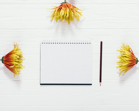 Composition of open blank notepad sheet among yellow and orange flowers on wooden table, top view....