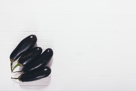 Raw eggplants on white wooden table, top view. Flat lay composition group of aubergine vegetables placed in corner, copy space.の写真素材