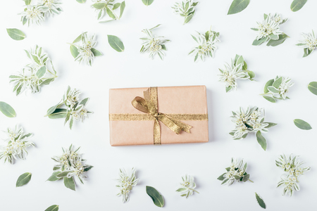 Gift box with gold ribbon bow in middle of green flowers pattern, flat lay composition. Top view on a present on white background.の写真素材