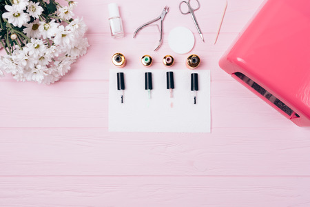 Set shellac covering: bottles gel nail polishes, brushes, ultraviolet lamp, tools and bouquet flowers, top view. Creative flatlay equipment long lasting manicure. Manicurist workplace on pink desk.の写真素材