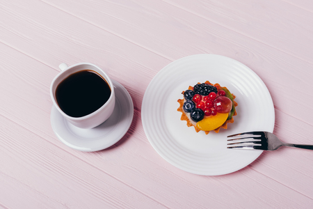 Delicious small berry cupcake on plate with fork and espresso on pink wooden table, top view. Cup of black coffee with dessert.の写真素材