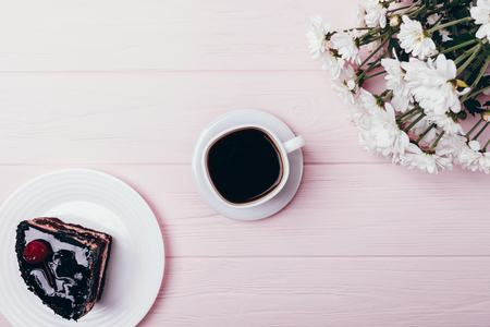 Floral composition piece chocolate cake and cup of espresso on pink wooden table, top view. Flat lay arrangement of black coffee, dessert and bouquet of fresh flowers.の写真素材