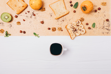 Flat lay healthy vegetarian breakfast composition. Cup of espresso coffee on white wooden table next to toast, fruits and nuts, top view.の写真素材