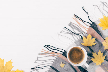 Top view cup of coffee among cozy flat lay  composition of autumn leaves and checkered fringe scarf on white wooden table, copy space.の写真素材