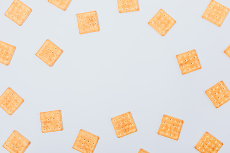 Pattern frame of yellow square crackers on white background, top view. Flat lay creative arrangement of salty cookies.の写真素材