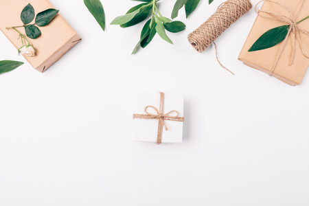 Small gift box on white background next to flat lay the top border of green leaves, presents and...