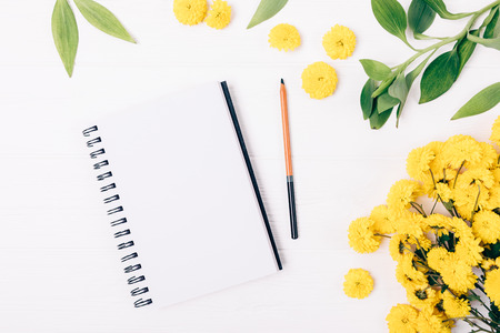 Spring flat lay composition open blank notepad and pencil next to decorative frame of yellow flowers and green leaves on white table, top view.の写真素材