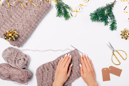 Festive Christmas flat lay composition woman's hands with manicure next to knitted wool sweater and needles, top view on white background.の写真素材