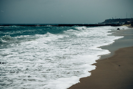 Landscape stormy sea coast with foamy waves and dark heavy sky. City beach during snowstorm at winter.の写真素材