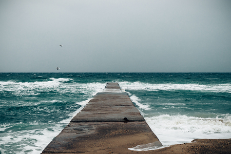Sea pier in gloomy stormy weather under heavy gray sky in winter.の写真素材
