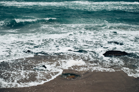 Beautiful seascape in rough weather, foamy waves roll on sandy beach with rocks.の写真素材