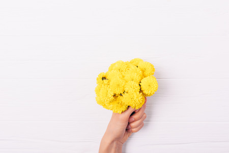 Small yellow bouquet in woman's hand on white wooden background, flat lay.の写真素材